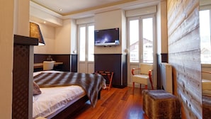 Habitación de hotel con cama, una silla, televisor montado en la pared y ventana con vistas a edificios.