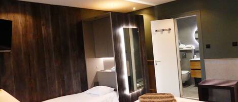 A hotel room with two single beds, a large mirror, a wardrobe, and a small desk with a chair.