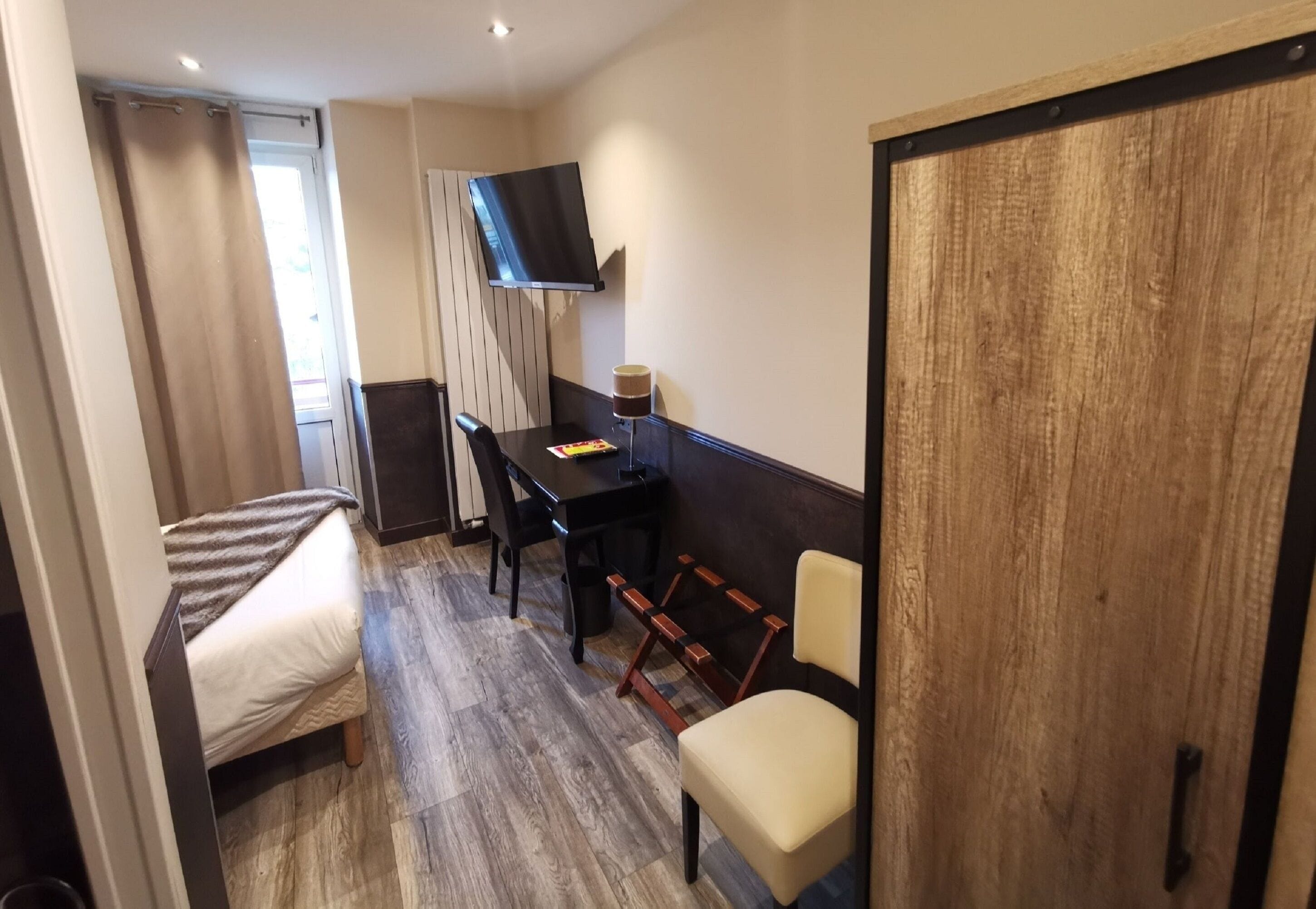A hotel room with a bed, a desk, a chair, a TV mounted on the wall, and a wooden door.