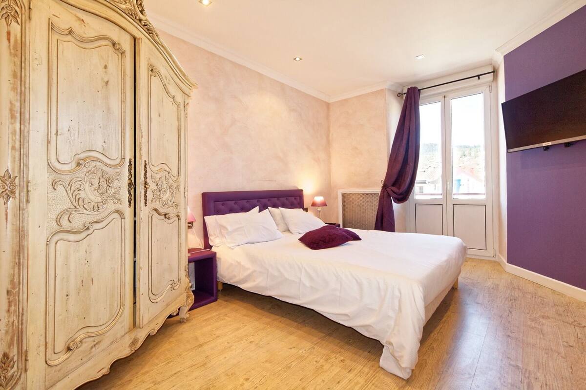 Un dormitorio con una cama grande, un armario, un televisor y una ventana con cortinas.