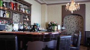 Zona de bar con mostrador, estanterías llenas de botellas de licor, un candelabro y una pared cubierta de papel tapiz floral.