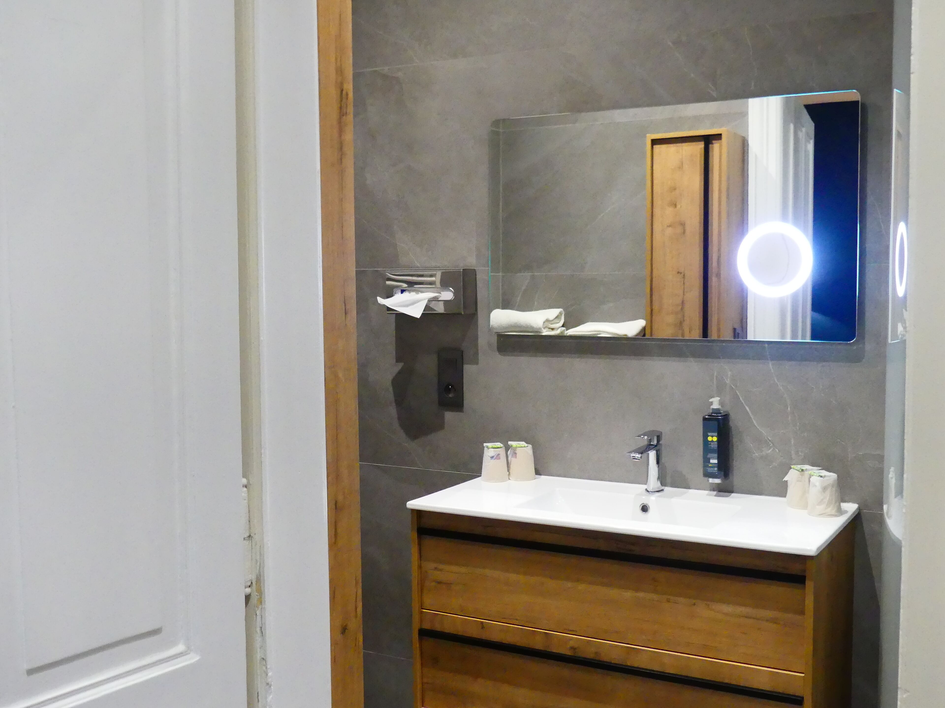 A bathroom with a white sink, wooden vanity, and a mirror with a light.