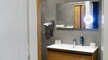 Un baño con lavamanos blanco, tocador de madera y espejo con luz.