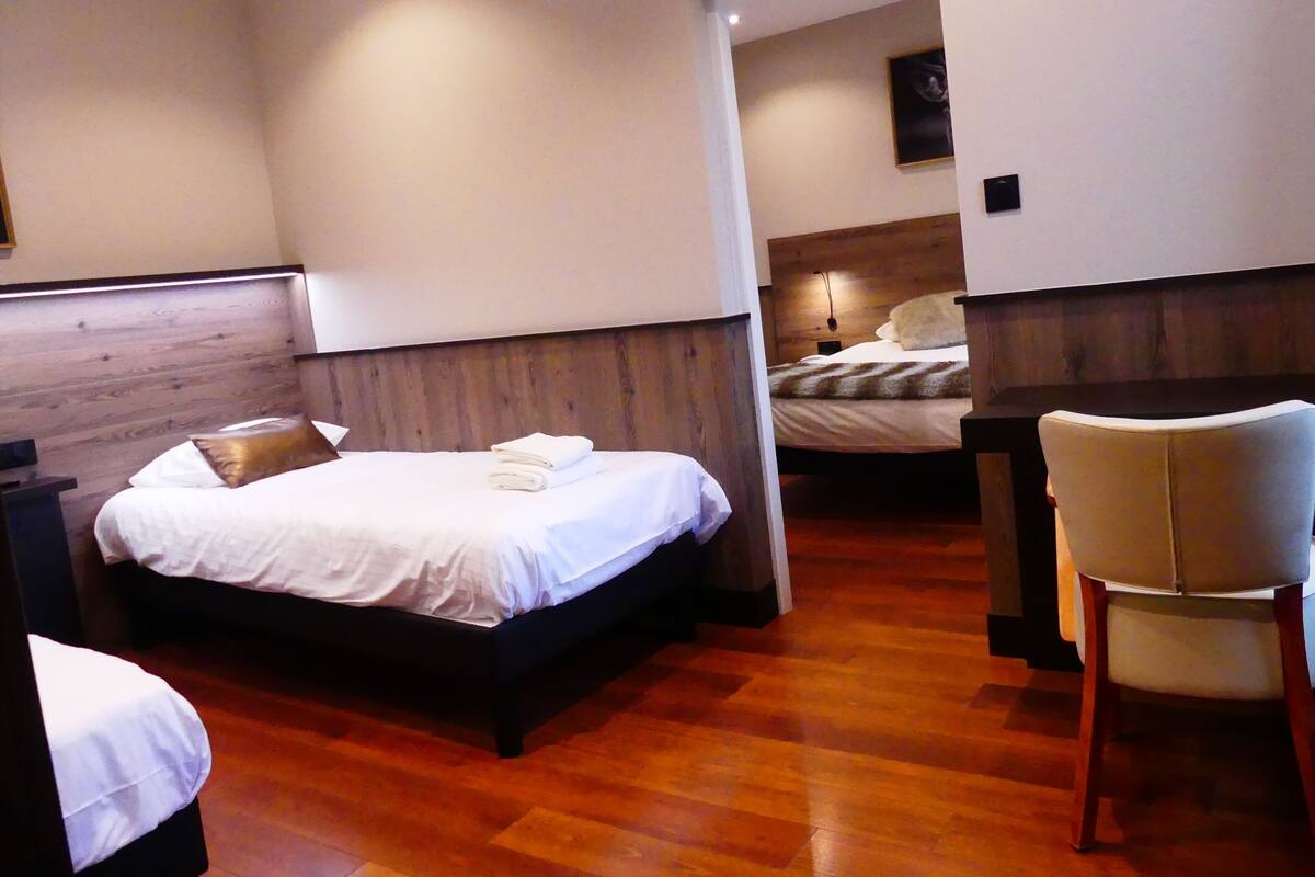 Una habitación de hotel con cabecera de madera, cama con ropa blanca, suelo de madera y un escritorio con silla.