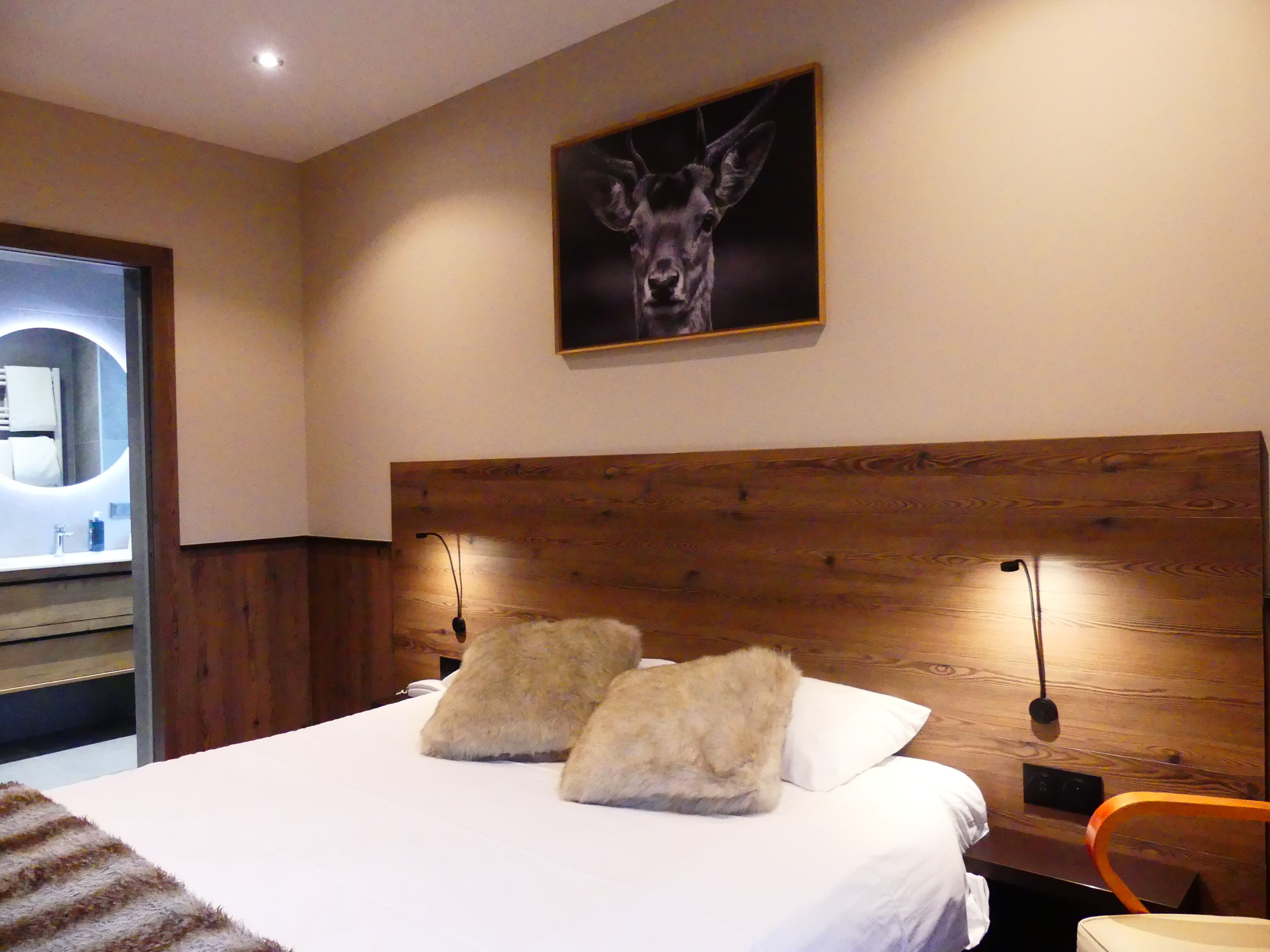 Une chambre d’hôtel avec une tête de lit en bois, deux oreillers, un lit, une table de chevet, une lampe et un tableau encadré au mur.