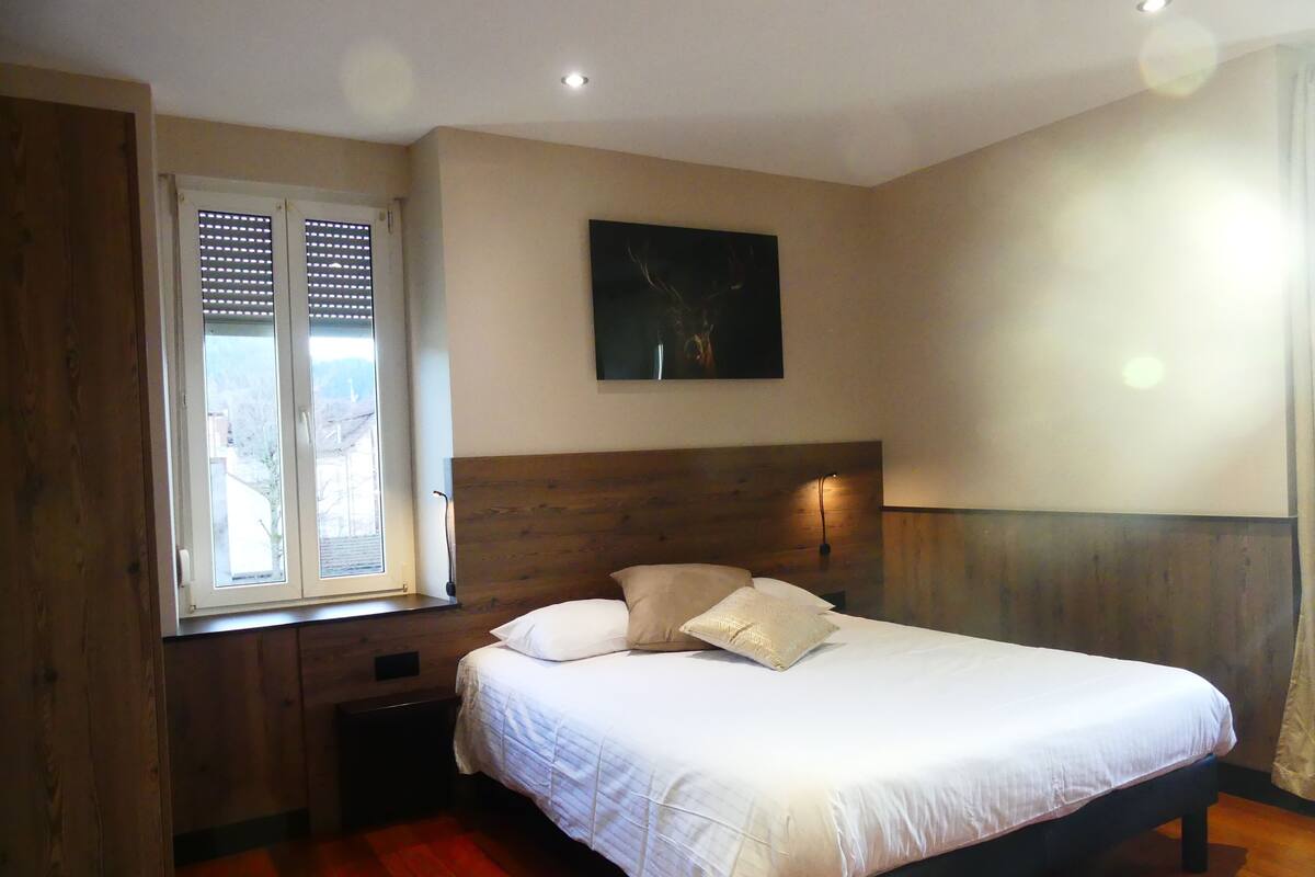 Un dormitorio con cama, cabecero de madera, ventana con persianas y un cuadro en la pared.