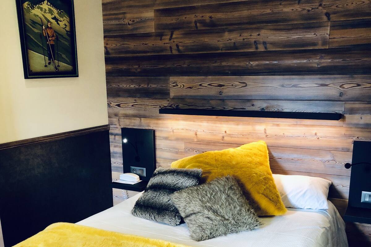 Una cama con una manta amarilla, un cojín gris y negro y un cojín amarillo.