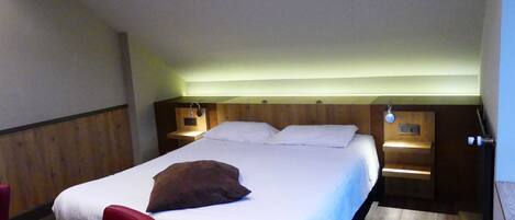 A single bed with a wooden headboard, two bedside tables with lamps, a red chair, and a wooden floor.