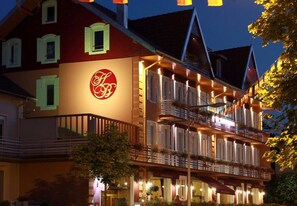 A hotel with a prominent logo, multiple balconies, and a well-lit facade. - Hotel des Bains (Gerardmer)