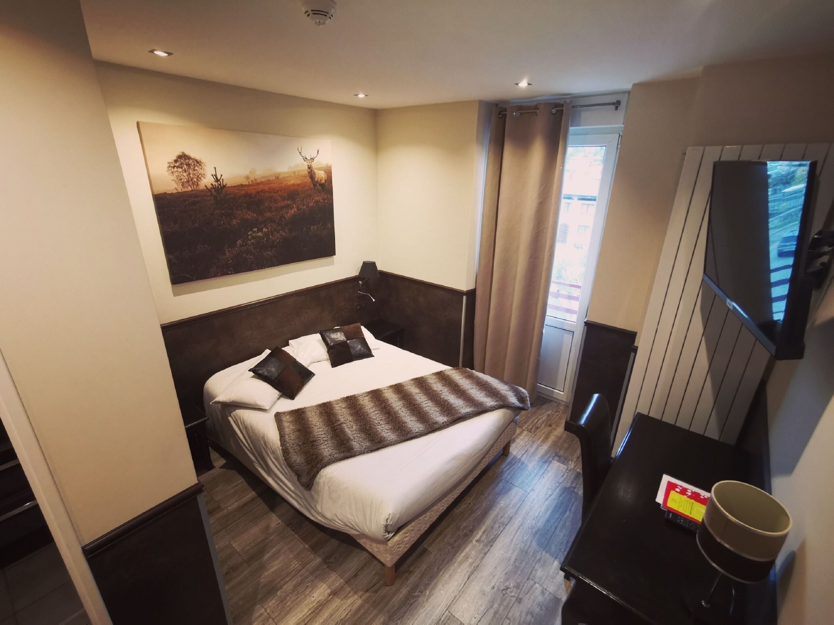 Ein Hotelzimmer mit einem Bett, einem Schreibtisch, einem Fernseher und einem Gemälde an der Wand.