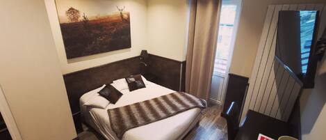 Una habitación de hotel con cama, escritorio, televisión y un cuadro en la pared.
