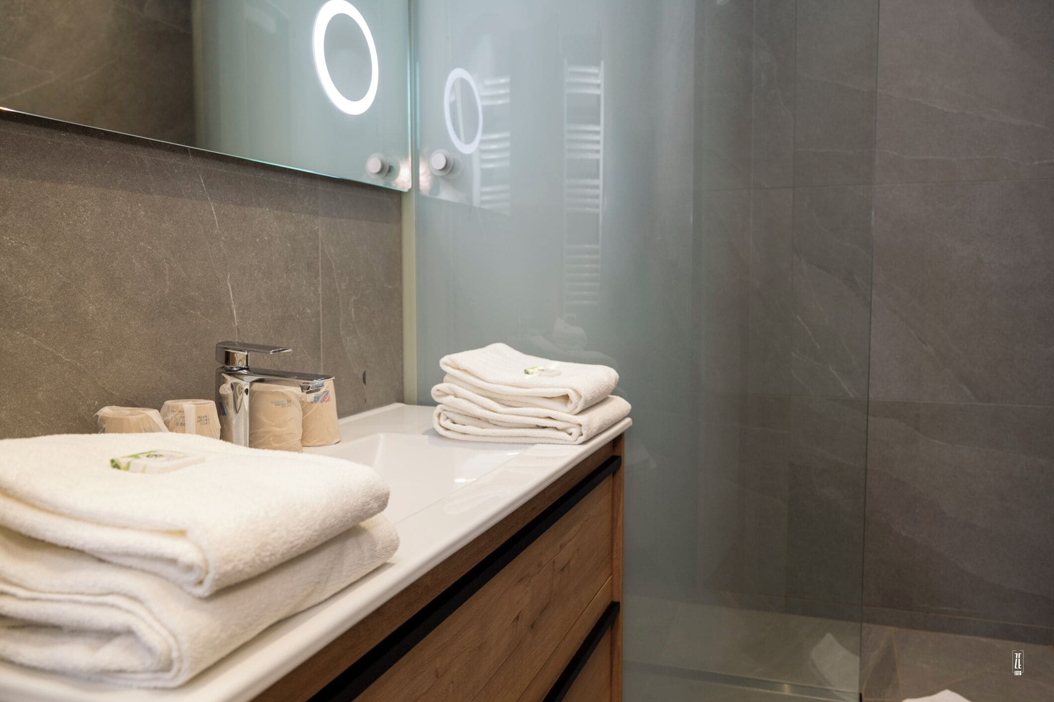 Un baño con lavamanos blanco, toallas apiladas y artículos de aseo.