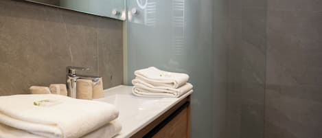 Un baño con lavamanos blanco, toallas apiladas y artículos de aseo.