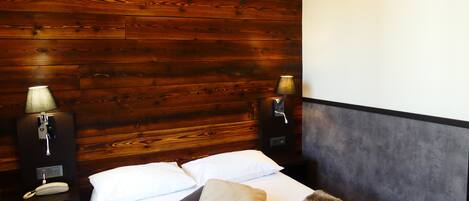 Habitación de hotel con cabecera de madera, cama con sábanas blancas, dos lámparas de noche y un teléfono en la mesita.