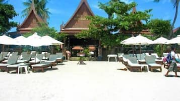 Un resort en la playa con un templo tailandés tradicional al fondo, tumbonas y sombrillas.