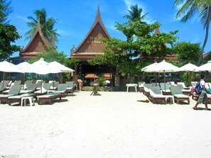 A beach resort with a traditional Thai temple in the background, sun loungers, and umbrellas.
