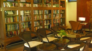 A library with wicker chairs and tables, a television, and bookshelves filled with books. - White House Beach Resort (Koh Samui)