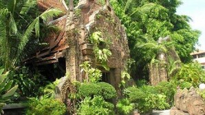 A stone structure surrounded by lush greenery, with a pathway leading to a stone statue. - White House Beach Resort (Koh Samui)