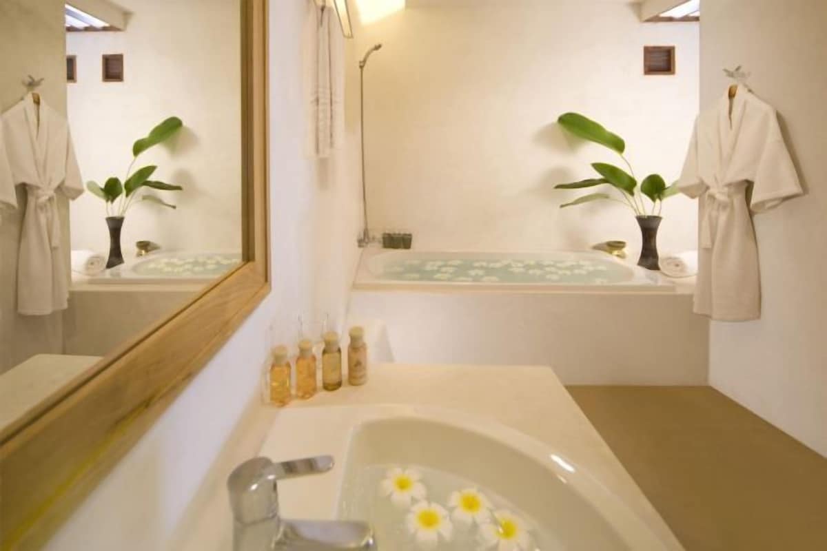Une salle de bain avec une baignoire, un lavabo, un miroir et deux plantes en pot.