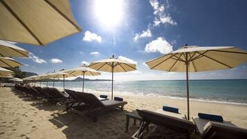 A beach with rows of sun loungers and large umbrellas, a clear sky, and the ocean in the background.