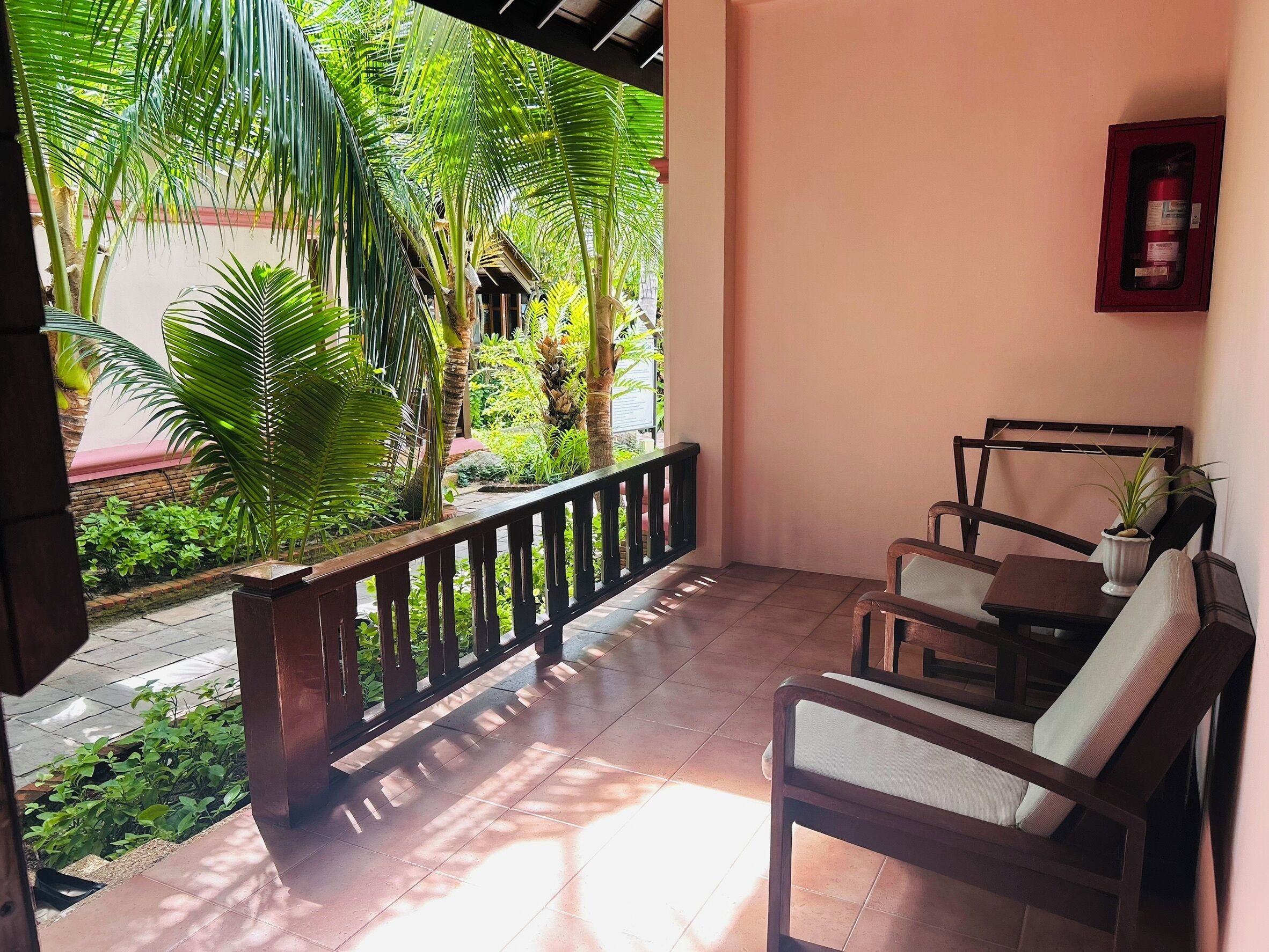A balcony with a wooden railing, a seating area with two chairs and a small table, and a fire extinguisher mounted on the wall.