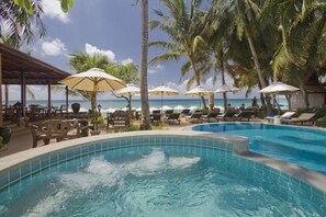 A pool area with lounge chairs and umbrellas, surrounded by palm trees and a view of the ocean.