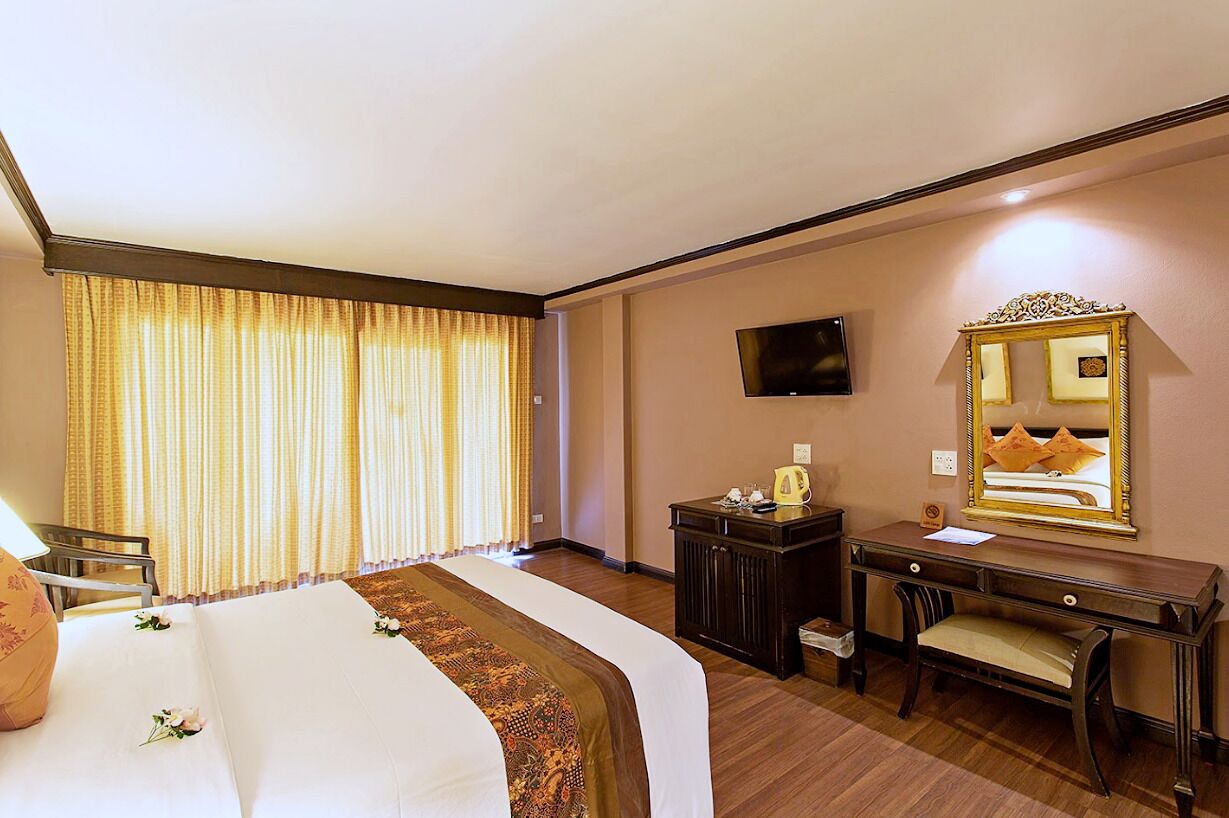 Una habitación de hotel con cama, escritorio, silla, televisor y espejo.