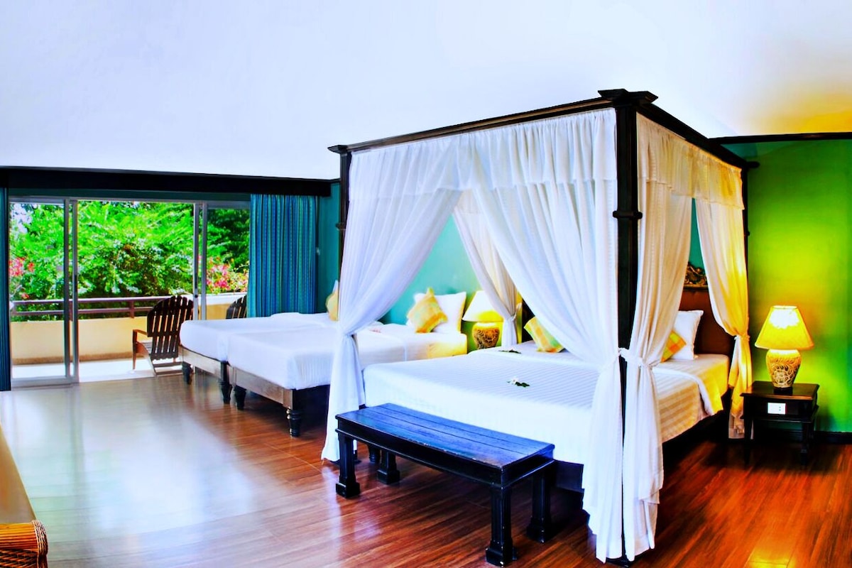 A room with two beds, a bench, and a view of greenery outside.