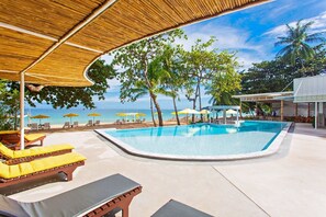 Un espace piscine aménagé avec des chaises longues, des parasols et une vue sur la plage et l’océan.