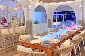 A dining area with a long wooden table, wicker chairs, and a sofa. - The Fair House Beach Resort & Hotel (Koh Samui)