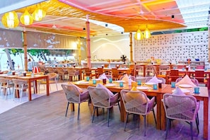 Un restaurant doté de plusieurs tables et chaises, d’un plafond orné de luminaires suspendus et d’un mur décoré de motifs.
