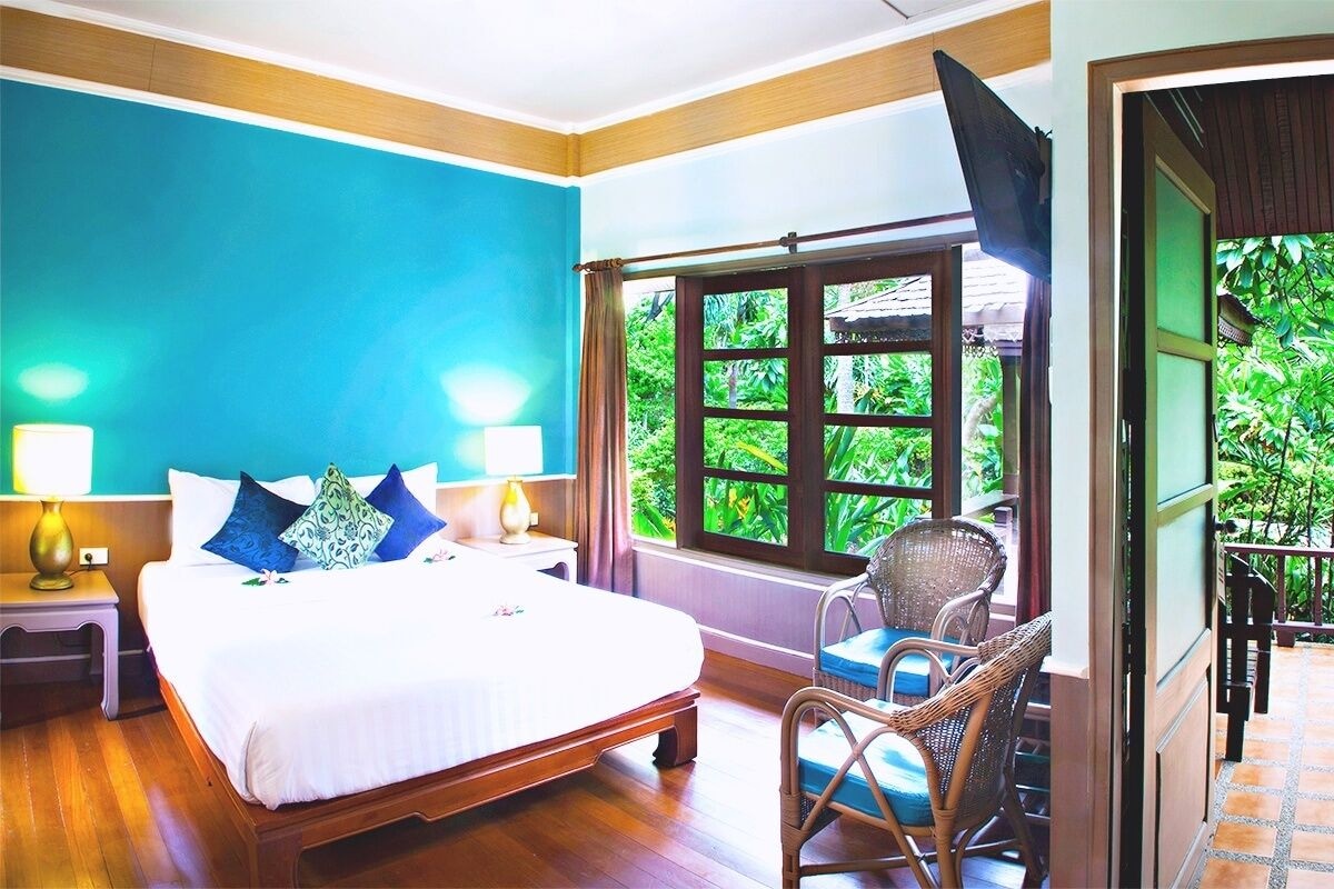 A bedroom with a bed, nightstands, a chair, a window with a view of greenery, and a television.