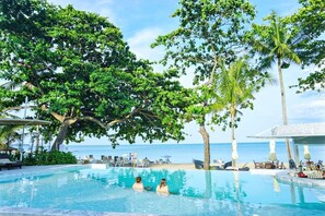 A pool with two people, surrounded by palm trees and a view of the ocean. - The Fair House Beach Resort & Hotel (Koh Samui)