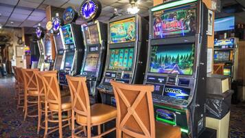 Una fila di slot machine con il logo 'WMS', sedie di legno e un tappeto a motivi.