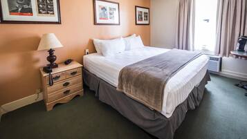 A hotel room with a large bed, a bedside table with a lamp, a dresser, and framed pictures on the wall.
