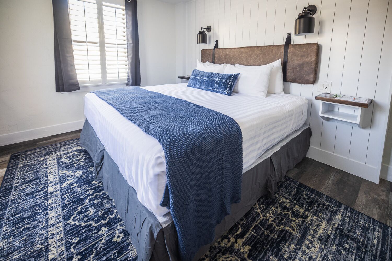 Una cama bien hecha con una colcha azul, un cabecero de madera y una mesita de noche con una lámpara.