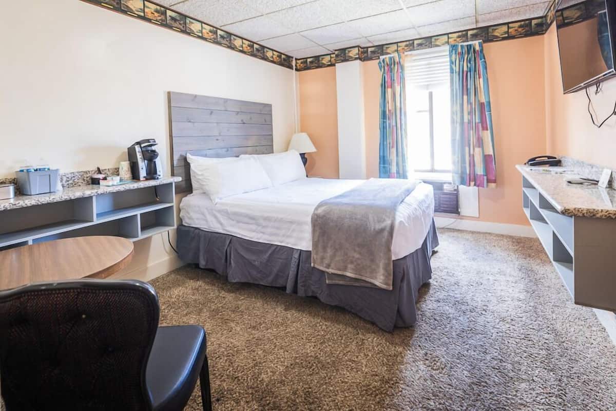 A hotel room with a bed, a desk, a chair, a TV, and a window with curtains.