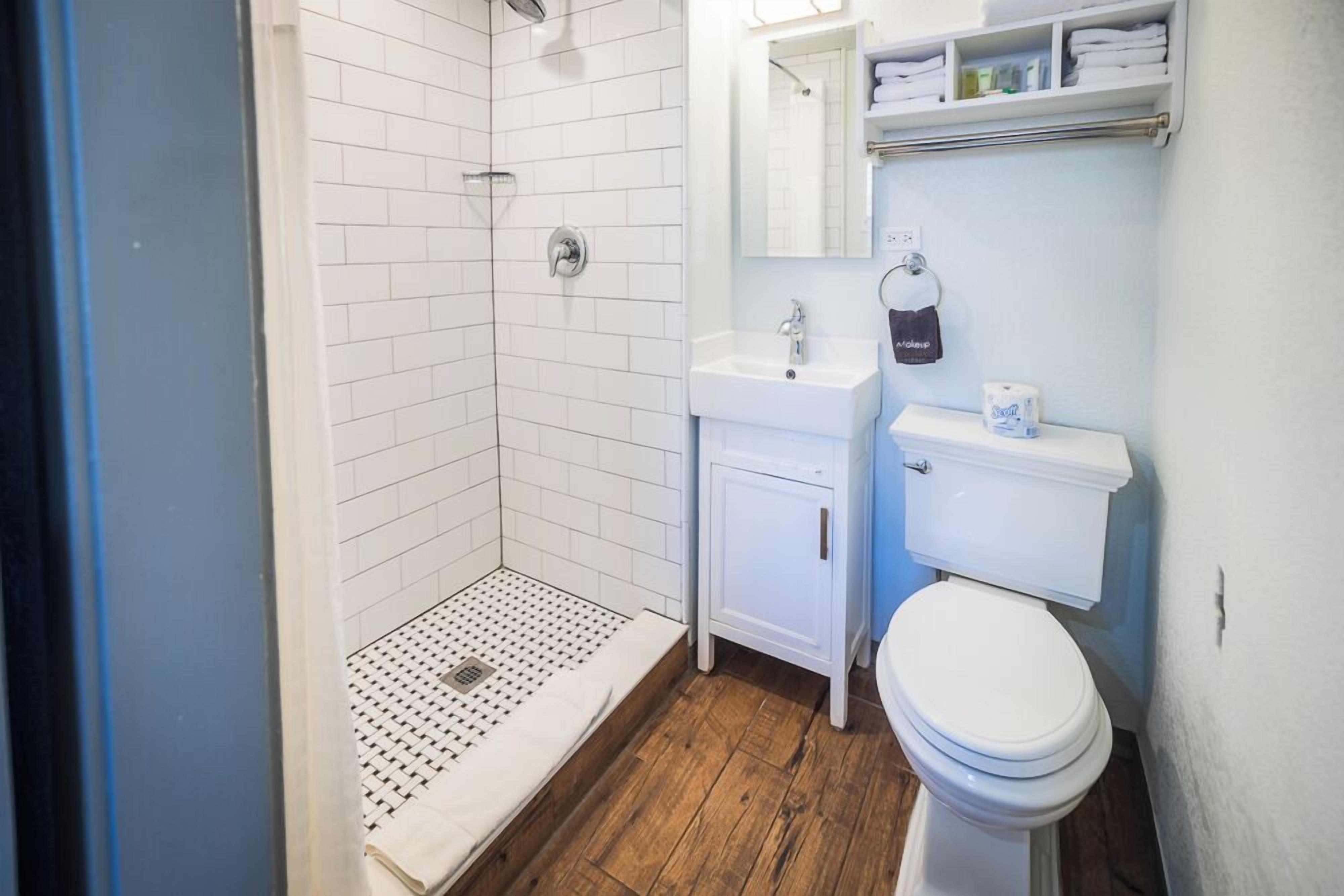 A bathroom with a shower, toilet, sink, and storage shelves.