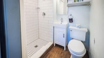 A bathroom with a shower, toilet, sink, and storage shelves.