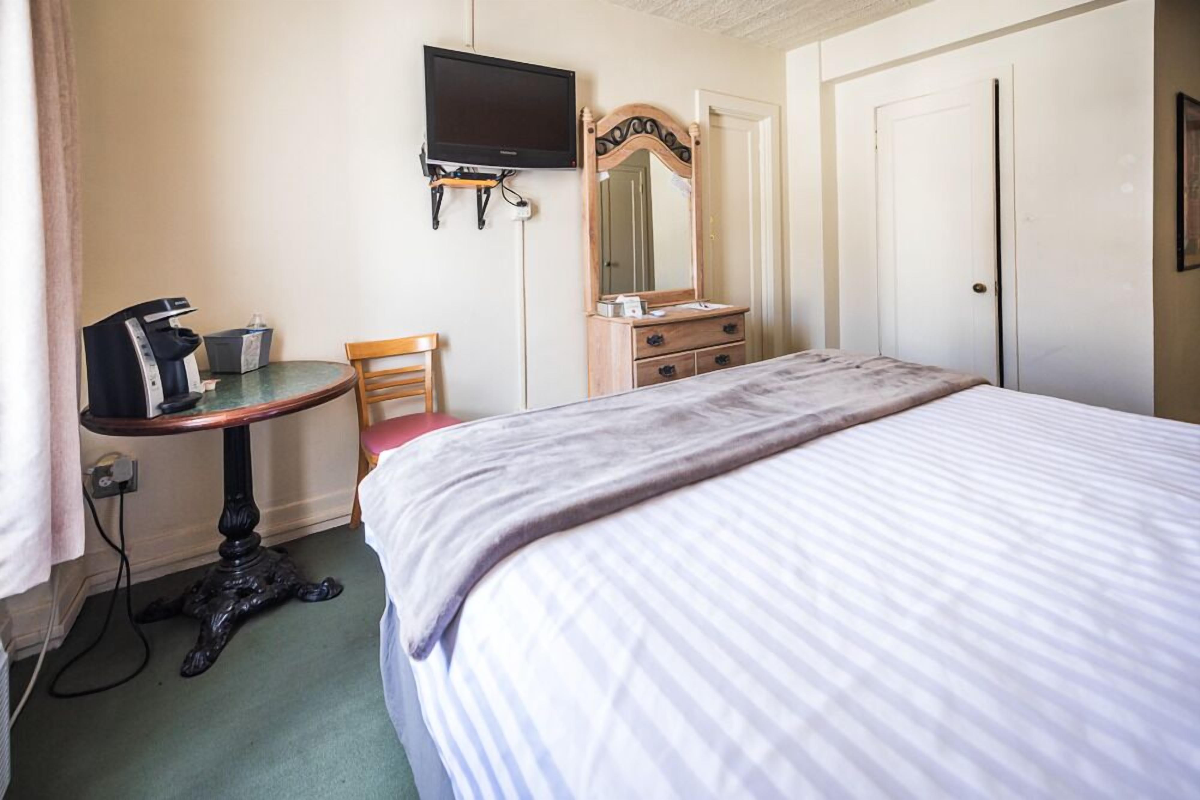Una camera d'albergo con un letto, una scrivania con una sedia, una televisione, un comò e uno specchio.