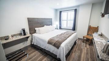 A compact bedroom with a bed, a window, a chair, and a small kitchenette area.
