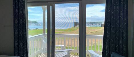 A room with a bed, a blue armchair, and a sliding glass door leading to a deck with outdoor furniture and a view of the sea.