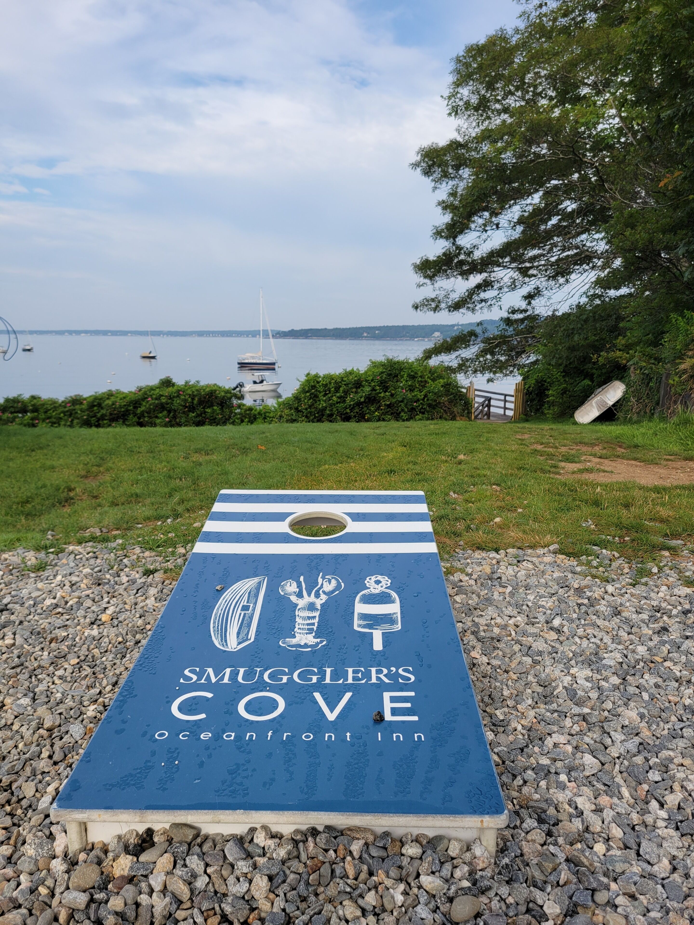 A blue sign for Smuggler's Cove Oceanfront Inn with a view of boats and a tree in the background.