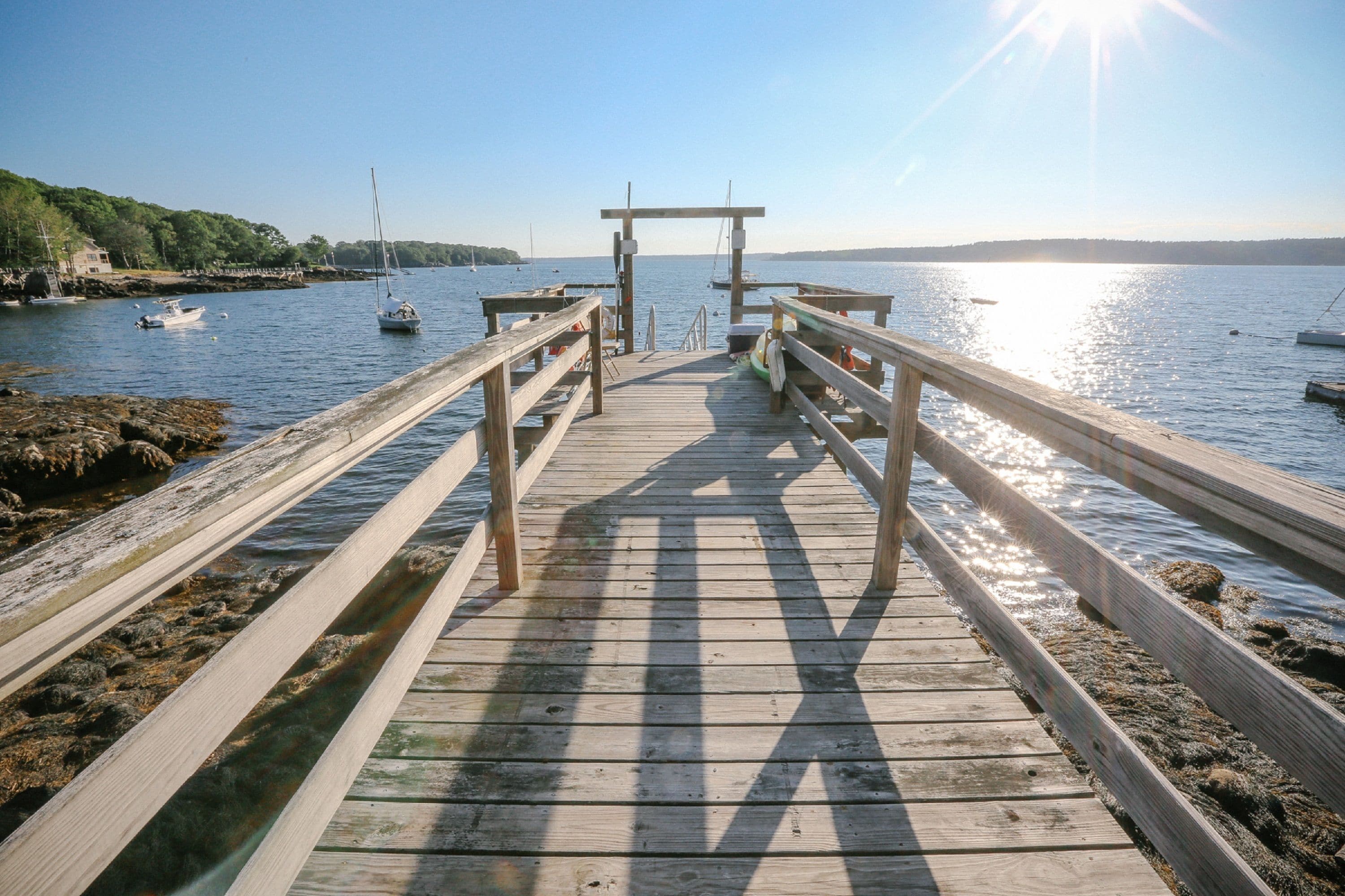 A wooden pier leading to a dock with a clear view of the water and boats.