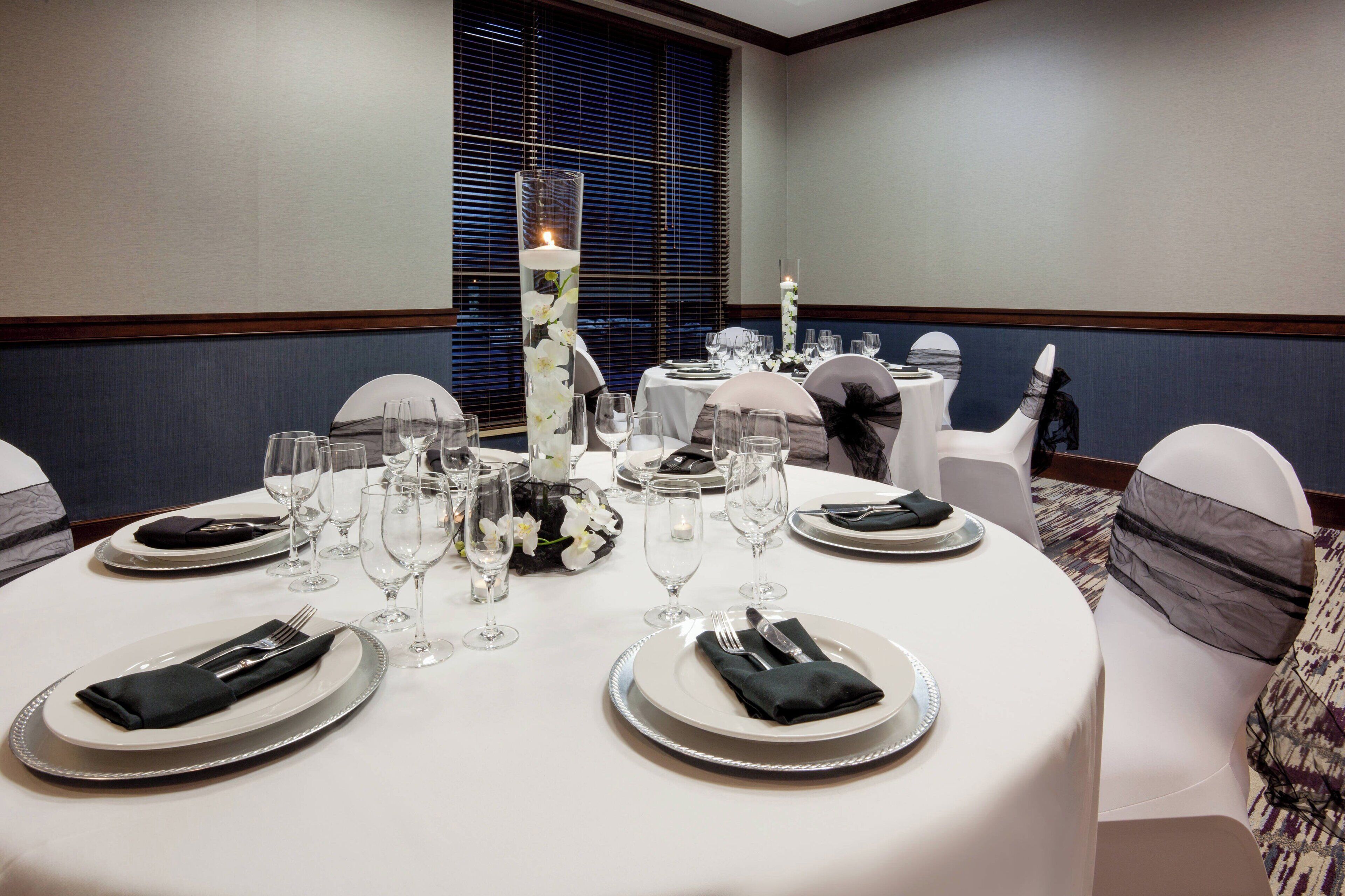A round dining table set with plates, cutlery, and glasses, surrounded by chairs with white and gray cushions.