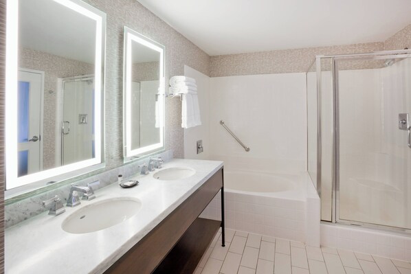 A modern bathroom with two sinks, a large mirror, a glass-enclosed shower, and a bathtub.