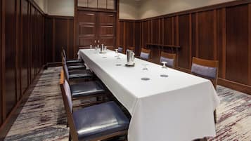 Un salón de conferencias con una larga mesa, sillas y un revestimiento de madera en la pared.