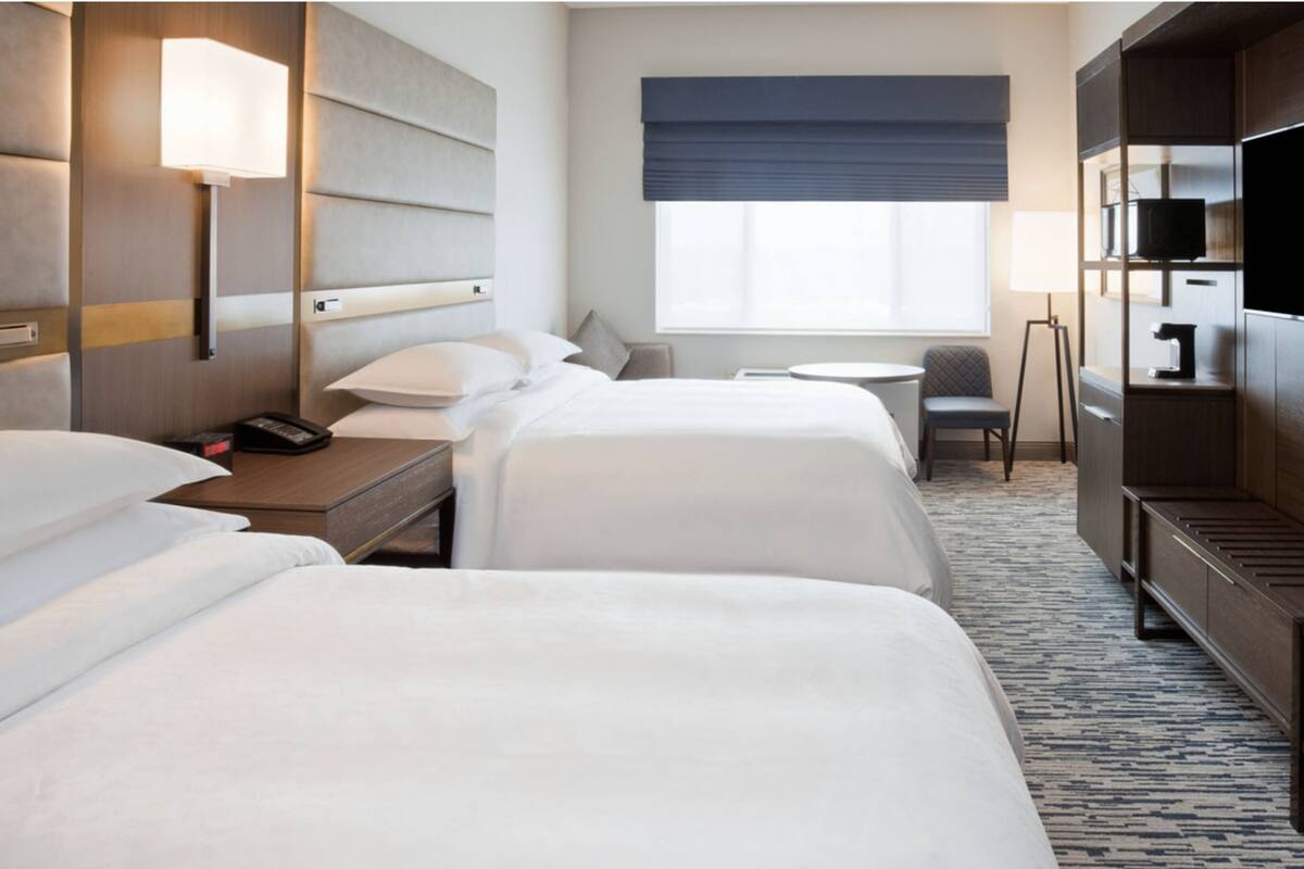 A hotel room with two beds, a desk, a chair, a TV, and a window with a view.
