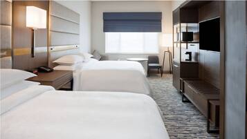 Une chambre d’hôtel avec deux lits, un bureau, une chaise, une télévision et une fenêtre donnant sur un paysage agréable.