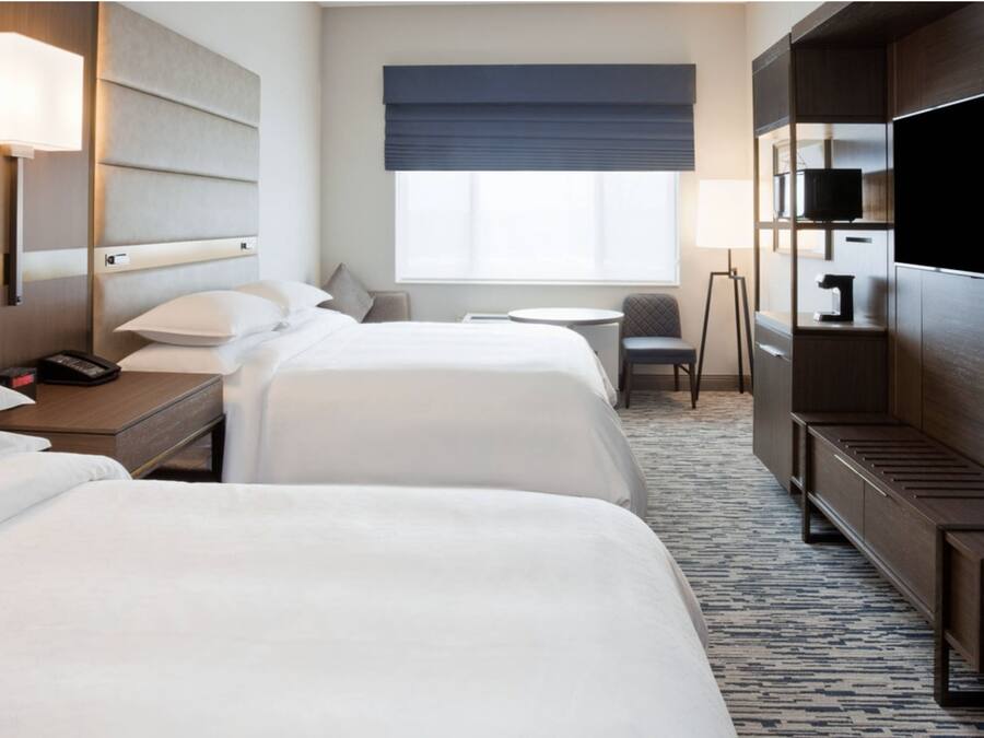 Une chambre d’hôtel avec deux lits, un bureau, une chaise, une télévision et une fenêtre donnant sur un paysage agréable.